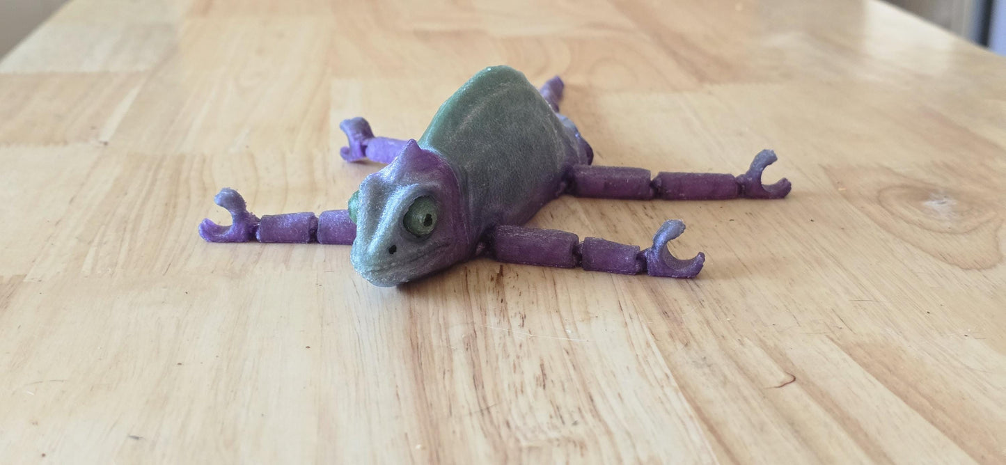 Articulated rubber chameleon laying flat on a table.