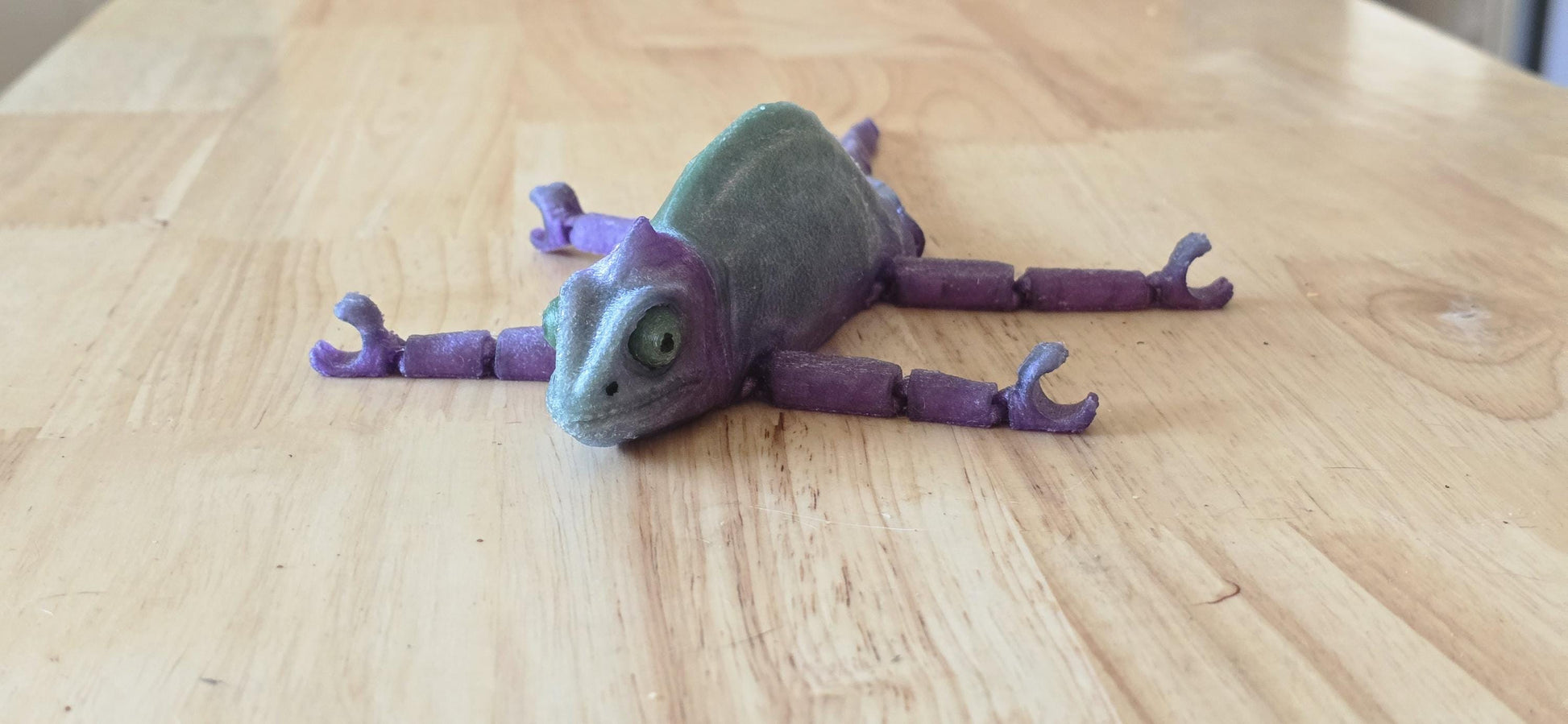 Articulated rubber chameleon laying flat on a table.