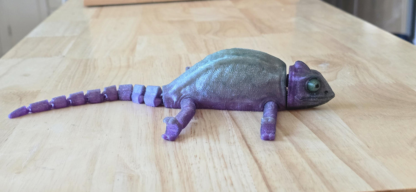 Articulated rubber chameleon laying flat on a table. side view.